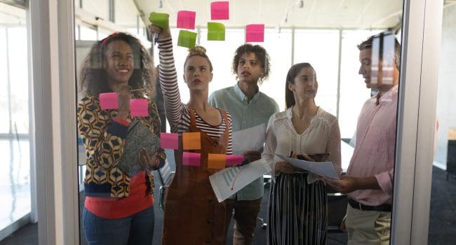 Front view of multi-ethnic business colleagues discussing business strategy over sticky notes in modern office