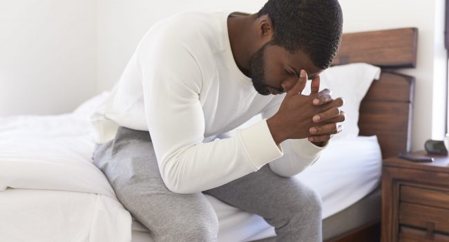 Depressed Man Looking Unhappy Sitting On Side Of Bed At Home With Head In Hands Depressed Man Looking Unhappy Sitting On Side Of Bed At Home With Head In Hands