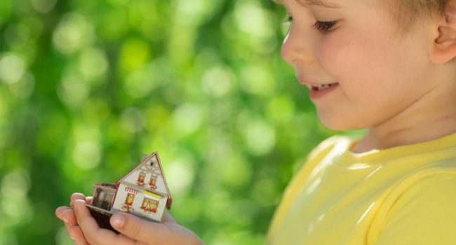 Child holding eco house in hands against spring green background. Real estate and Earth day holiday concept