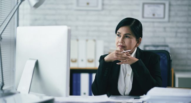 Pensive Vietnamese female attorney sitting in front of computer