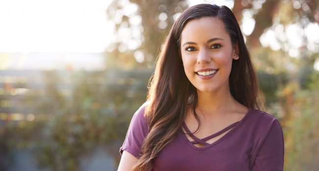 Portrait Of Smiling Hispanic Woman In Garden At Home Against Flaring Sun