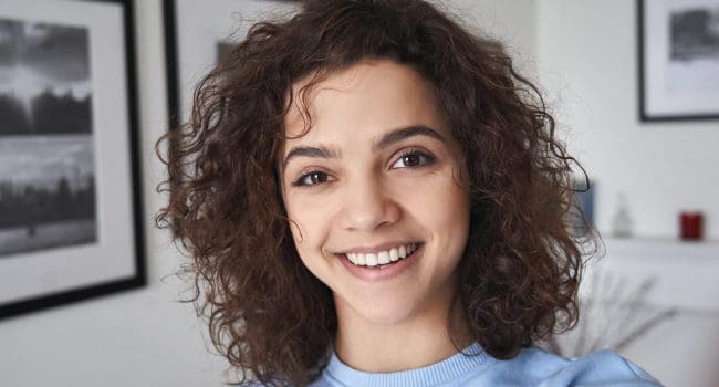 Smiling cute cheerful young pretty hispanic latin woman looking at camera. Smiling cute cheerful young pretty hispanic latin woman looking at camera standing alone at home. Happy positive beautiful 20s girl female model posing indoors, close up face headshot portrait.