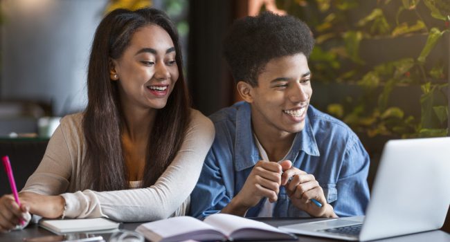 Teen mixed race couple of students enjoying studying at cafe, looking at laptop, making notes, free space