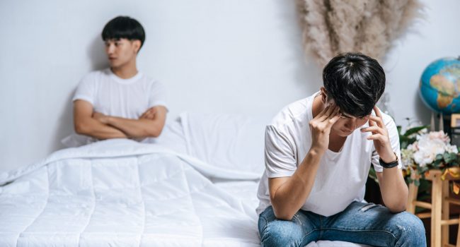 Two young men were angry on the bed and the other sat at the edg Two young men were angry on the bed and the other sat at the edge of the bed and was stressed.