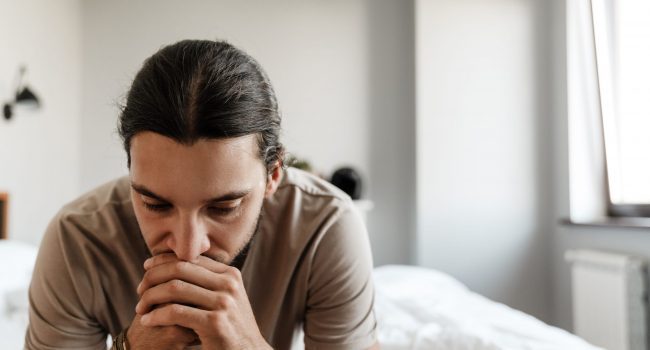 Young man in depression sitting on bed at home